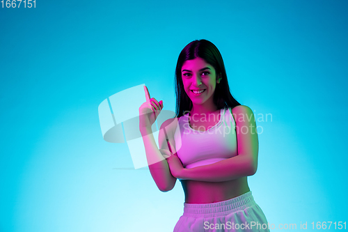 Image of Brunette beautiful woman\'s portrait isolated on blue studio background in multicolored neon light