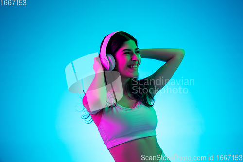 Image of Brunette beautiful woman\'s portrait isolated on blue studio background in multicolored neon light