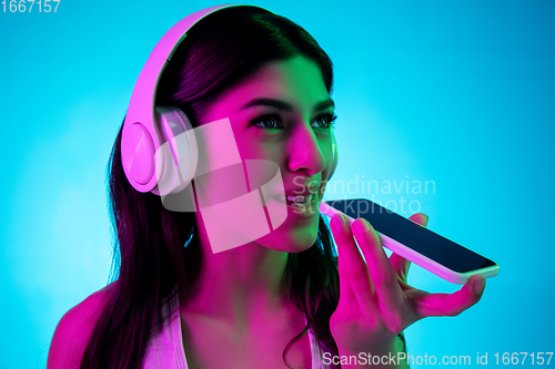 Image of Brunette beautiful woman\'s portrait isolated on blue studio background in multicolored neon light