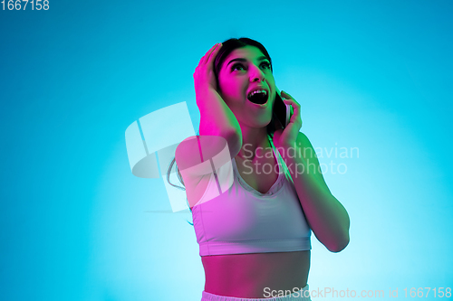 Image of Brunette beautiful woman\'s portrait isolated on blue studio background in multicolored neon light. Talking phone.