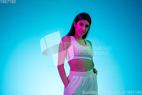 Image of Brunette beautiful woman\'s portrait isolated on blue studio background in multicolored neon light