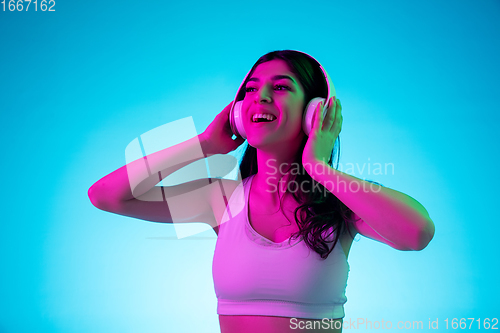 Image of Brunette beautiful woman\'s portrait isolated on blue studio background in multicolored neon light