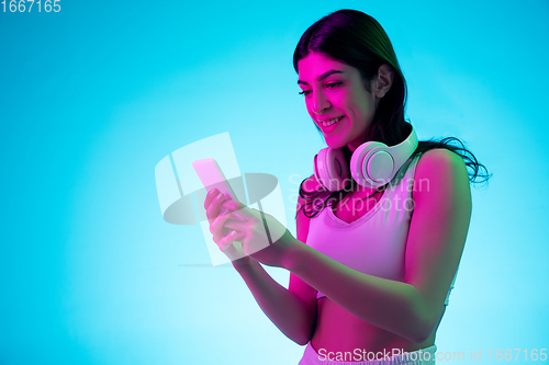 Image of Brunette beautiful woman\'s portrait isolated on blue studio background in multicolored neon light