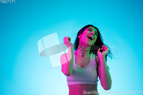 Image of Brunette beautiful woman\'s portrait isolated on blue studio background in multicolored neon light