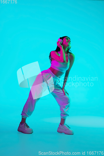 Image of Brunette beautiful woman\'s portrait isolated on blue studio background in multicolored neon light. Dancing with headphones