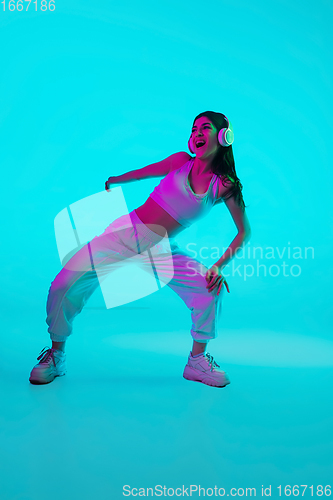 Image of Brunette beautiful woman\'s portrait isolated on blue studio background in multicolored neon light. Dancing with headphones