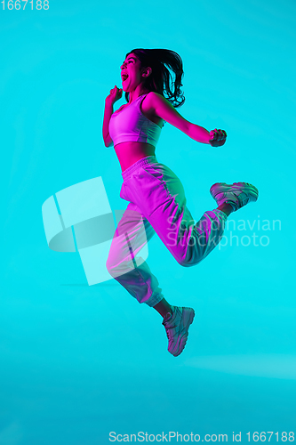 Image of Brunette beautiful woman\'s portrait isolated on blue studio background in multicolored neon light. Jumping high. flying