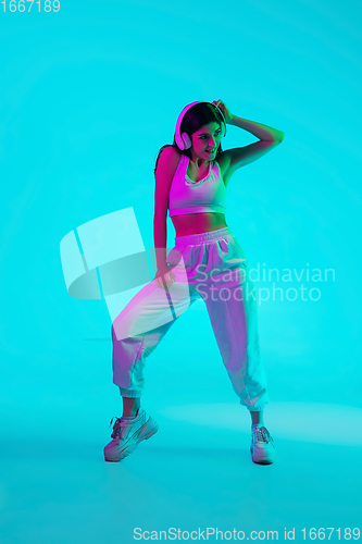 Image of Brunette beautiful woman\'s portrait isolated on blue studio background in multicolored neon light. Dancing with headphones