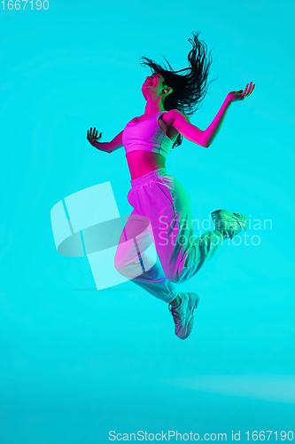 Image of Brunette beautiful woman\'s portrait isolated on blue studio background in multicolored neon light. Jumping high. flying