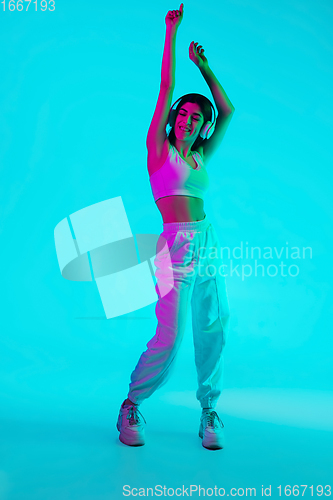 Image of Brunette beautiful woman\'s portrait isolated on blue studio background in multicolored neon light. Dancing with headphones