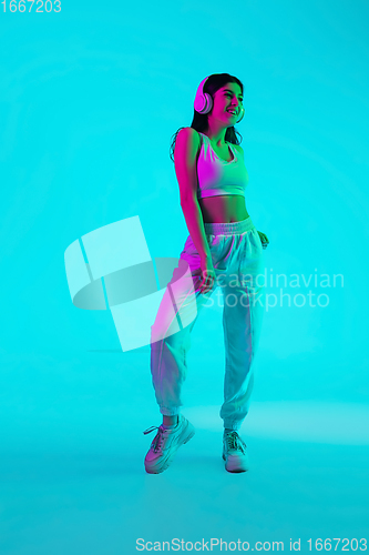 Image of Brunette beautiful woman\'s portrait isolated on blue studio background in multicolored neon light. Dancing with headphones