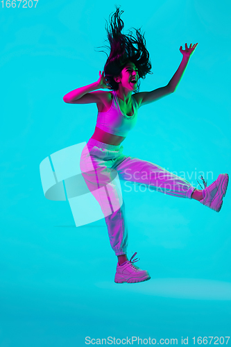 Image of Brunette beautiful woman\'s portrait isolated on blue studio background in multicolored neon light. Jumping high. flying