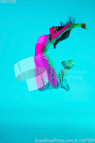 Image of Brunette beautiful woman\'s portrait isolated on blue studio background in multicolored neon light. Jumping high. flying