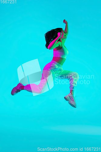 Image of Brunette beautiful woman\'s portrait isolated on blue studio background in multicolored neon light. Jumping high. flying