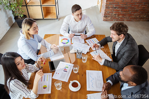 Image of Diverse group of co-workers having casual discussion in office. Executives during friendly discussion, month reporting, creative meeting. Top view.