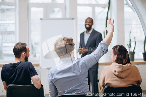 Image of Male speaker giving presentation in hall at workshop. Audience or conference hall. Rear view of unrecognized participants.