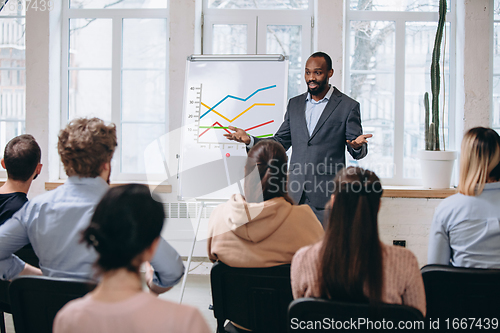 Image of Male speaker giving presentation in hall at workshop. Audience or conference hall. Rear view of unrecognized participants.