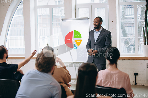 Image of Male speaker giving presentation in hall at workshop. Audience or conference hall. Rear view of unrecognized participants.