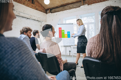 Image of Female speaker giving presentation in hall at workshop. Audience or conference hall. Rear view of unrecognized participants.