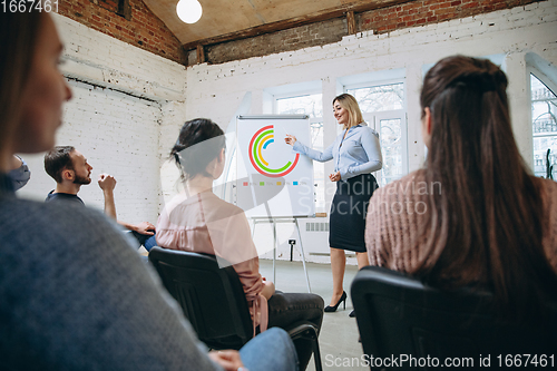 Image of Female speaker giving presentation in hall at workshop. Audience or conference hall. Rear view of unrecognized participants.