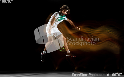 Image of Young caucasian professional sportsman playing tennis on black background in mixed light