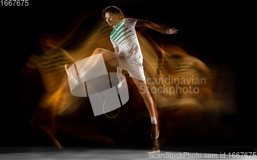 Image of Young caucasian professional sportsman playing tennis on black background in mixed light