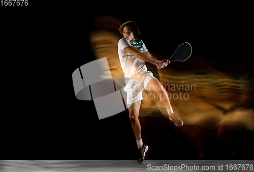 Image of Young caucasian professional sportsman playing tennis on black background in mixed light