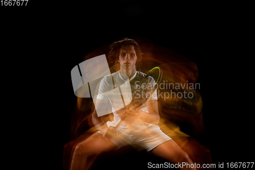 Image of Young caucasian professional sportsman playing tennis on black background in mixed light