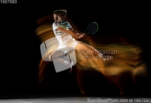 Image of Young caucasian professional sportsman playing tennis on black background in mixed light