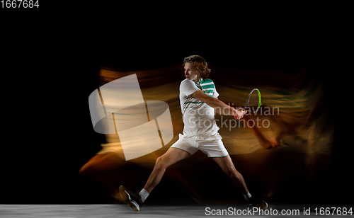 Image of Young caucasian professional sportsman playing tennis on black background in mixed light