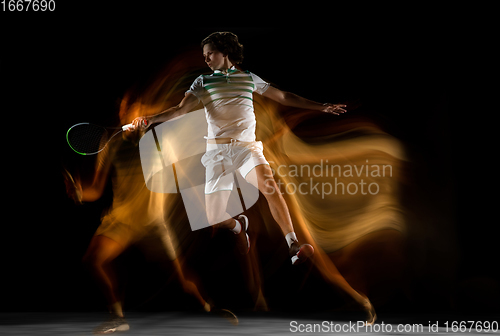 Image of Young caucasian professional sportsman playing tennis on black background in mixed light