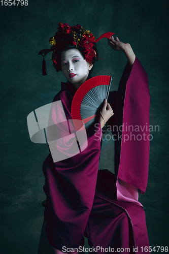 Image of Young japanese woman as geisha on dark green background. Retro style, comparison of eras concept.