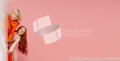 Image of Happy children isolated on coral pink studio background. Look happy, cheerful, sincere. Copyspace. Childhood, education, emotions concept