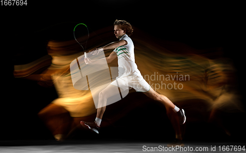 Image of Young caucasian professional sportsman playing tennis on black background in mixed light