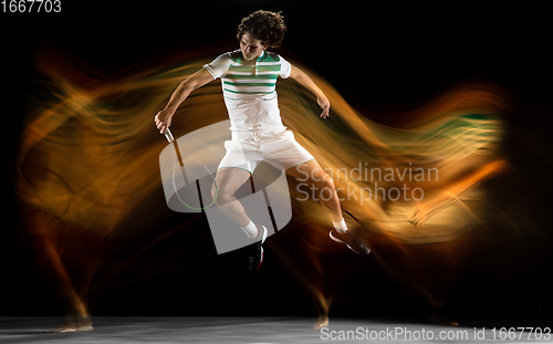 Image of Young caucasian professional sportsman playing tennis on black background in mixed light