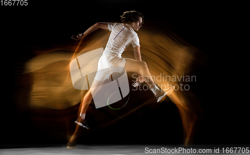 Image of Young caucasian professional sportsman playing tennis on black background in mixed light