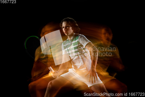 Image of Young caucasian professional sportsman playing tennis on black background in mixed light