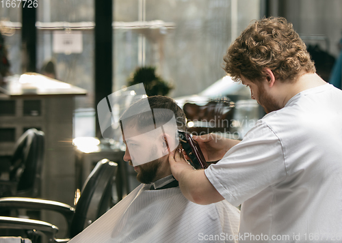 Image of Close up master barber, stylist does the hairstyle to guy, young man. Professional occupation, male beauty concept