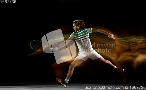 Image of Young caucasian professional sportsman playing tennis on black background in mixed light