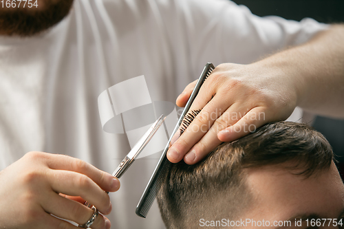 Image of Close up hands of master barber, stylist does the hairstyle to guy, young man. Professional occupation, male beauty concept