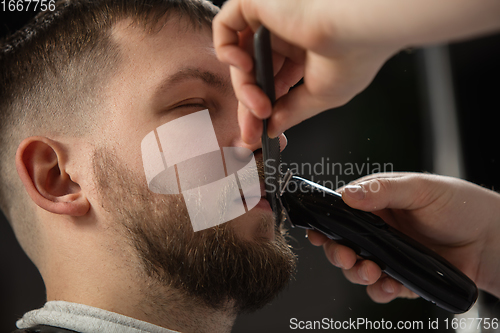Image of Close up of client of master barber, stylist during getting care of mustache and beard. Professional occupation, male beauty concept