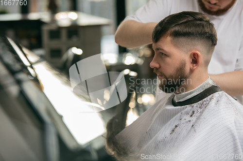 Image of Close up master barber, stylist does the hairstyle to guy, young man. Professional occupation, male beauty concept
