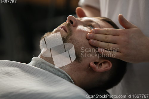 Image of Close up of client of master barber, stylist during getting care of mustache and beard. Professional occupation, male beauty concept