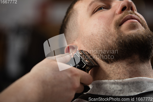 Image of Close up of client of master barber, stylist during getting care of mustache and beard. Professional occupation, male beauty concept