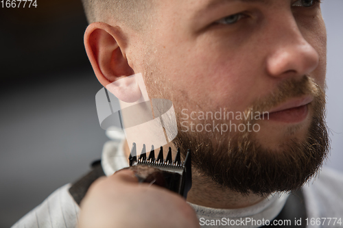 Image of Close up of client of master barber, stylist during getting care of mustache and beard. Professional occupation, male beauty concept