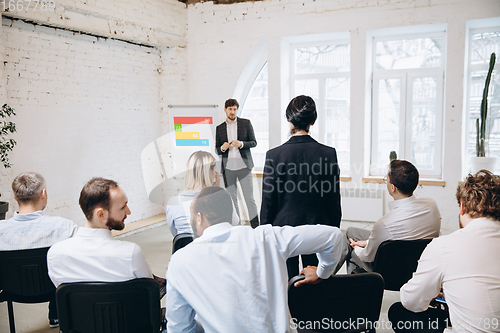 Image of Male speaker giving presentation in hall at workshop. Audience or conference hall. Rear view of unrecognized participants.