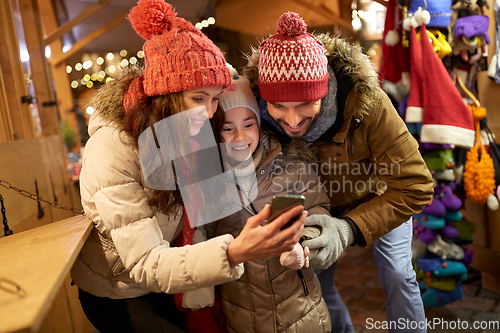 Image of happy family with smartphone at christmas market