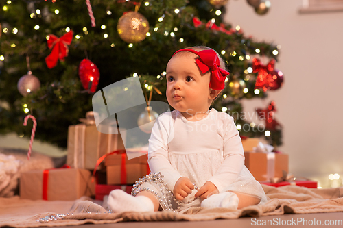 Image of baby girl at christmas tree with gifts at home