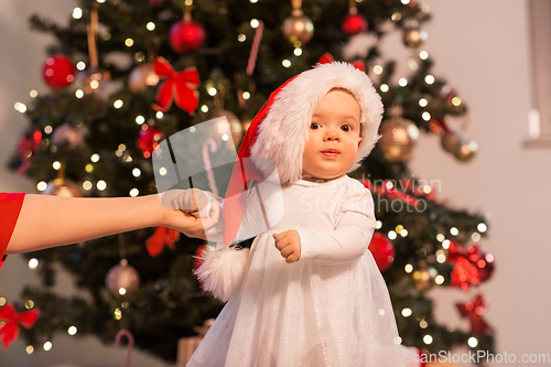 Image of baby girl with mother over christmas tree at home