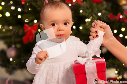 Image of baby girl with gift over christmas tree at home